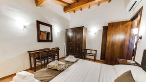 Una habitación de hotel con cama, armario de madera, escritorio y sillas, y un espejo.