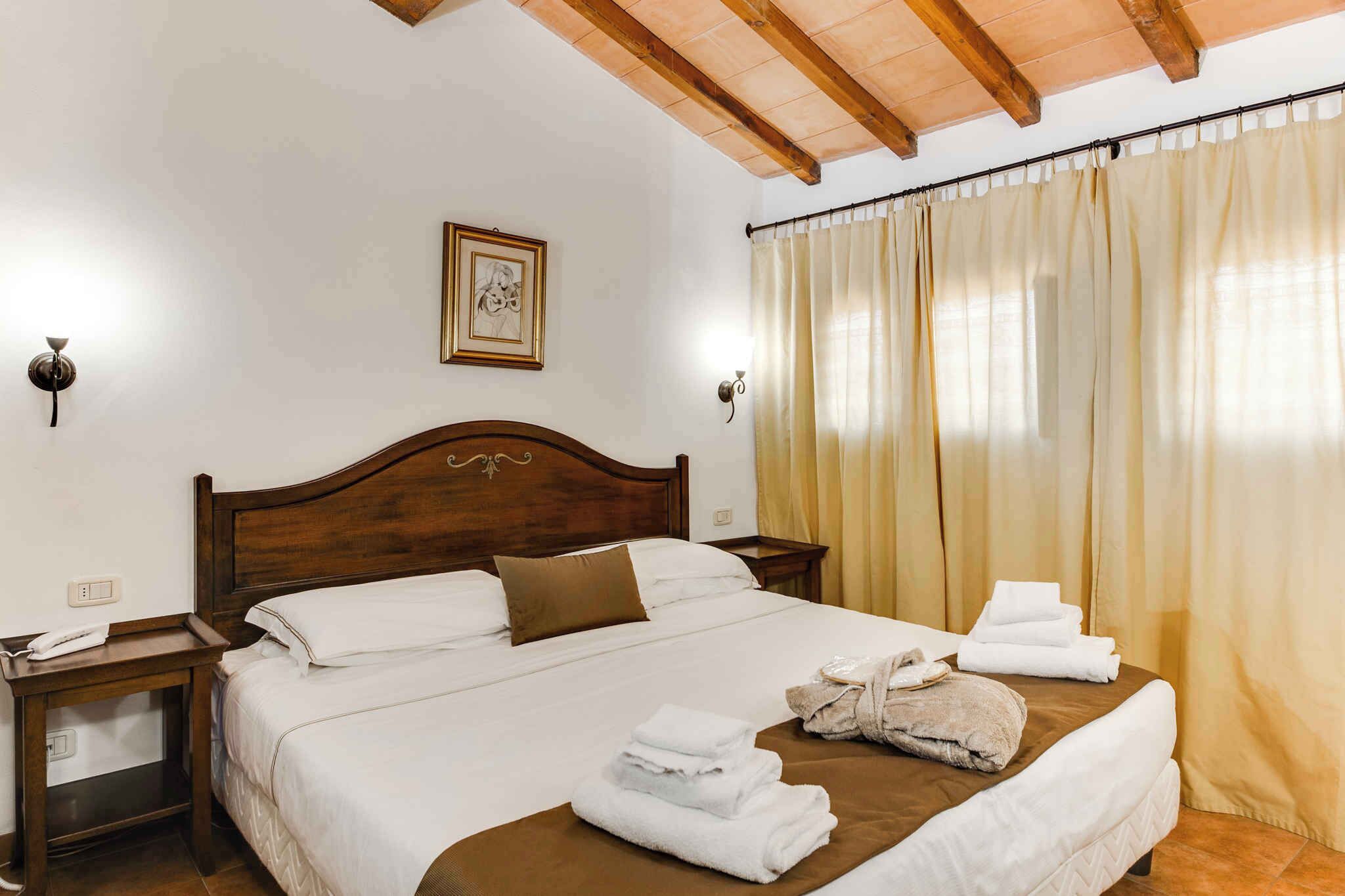 A hotel room with a wooden headboard, a bed with white linens, a brown pillow, a bedside table with a phone, and a window with beige curtains.