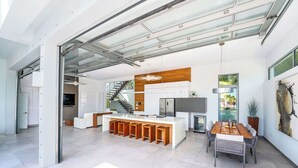 Eine moderne Küche mit einer zentralen Kochinsel, einem Essbereich mit Holztisch und einer Treppe, die in ein Obergeschoss führt.