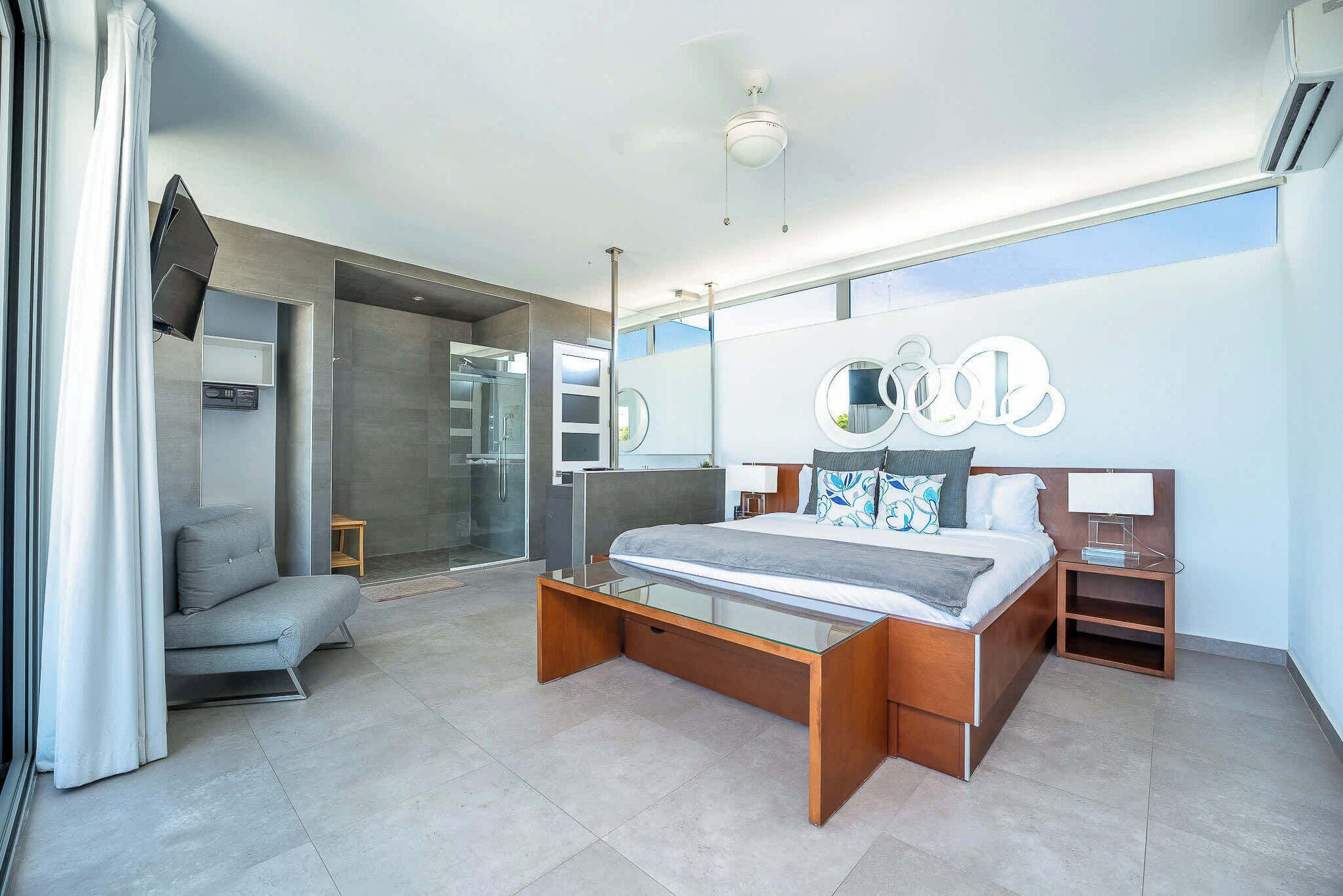 Una habitación de hotel moderna con una cama grande, un escritorio de vidrio, una zona de estar y vistas al exterior.