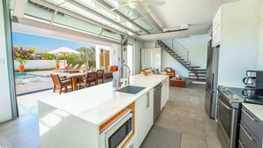 Een moderne keuken met een groot eiland, inbouwapparatuur en uitzicht op het buitenzwembad.