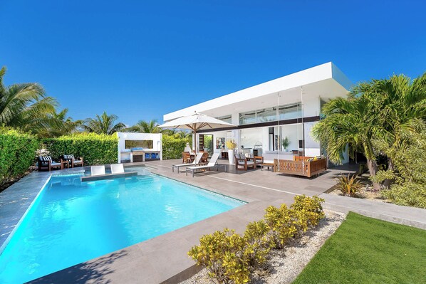 A modern house with a swimming pool, outdoor furniture, and lush greenery.