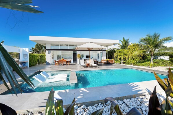 A modern house with a swimming pool, outdoor furniture, and tropical plants.