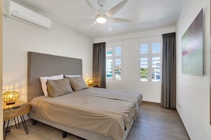 Une chambre d’hôtel équipée d’un lit, d’un ventilateur de plafond, d’un climatiseur, d’une fenêtre avec des rideaux et d’un téléviseur fixé au mur.