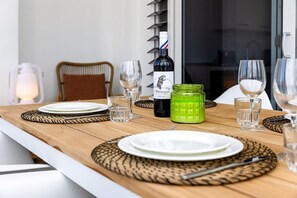 Et spisebord dækket med tallerkener, bestik og glas, samt en vinflaske og en grøn krukke.