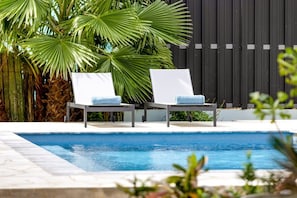 A swimming pool with two lounge chairs and a palm tree. - Liv Inn Bonaire with Pool and Nice Cooling Winds (Kralendijk)