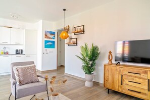 En moderne stue med sofa, fjernsyn, et træskab og en potteplante.