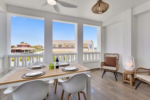 Un balcon avec une table à manger pour deux personnes, des chaises blanches et un fauteuil en osier.