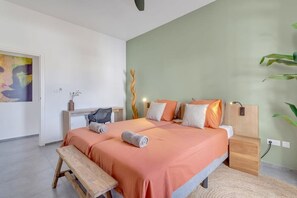 A bedroom with a bed, bedside tables, a bench, and a wall with a painting. - Belnem Breeze Kas di Mars with Communal Pool (Kralendijk)