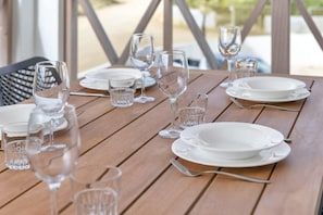 A wooden table set with white plates, clear glasses, and wine glasses, indicating a dining area. - Belnem Breeze Kas di Mars with Communal Pool (Kralendijk)