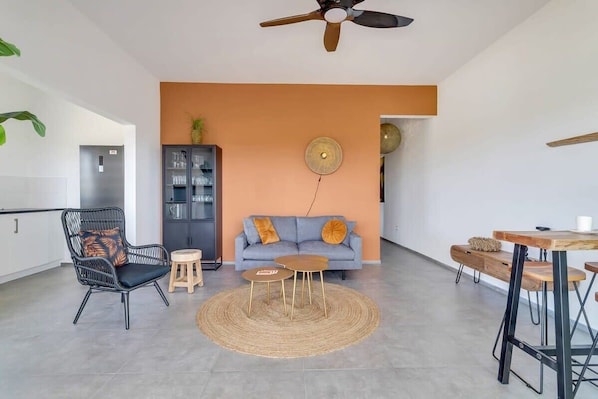 A modern living room with a sofa, a chair, a small table, and a ceiling fan.