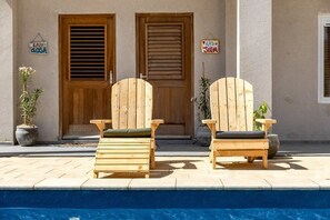 Ett område vid poolen med två träloungestolar och en skylt som visar vilka rum som finns.