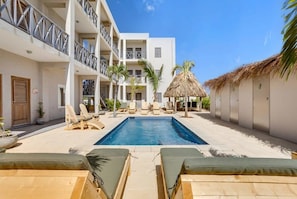 A hotel courtyard with a swimming pool, lounge chairs, and a thatched-roof structure.