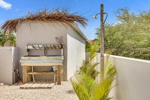 A small outdoor area with a wooden bench, a thatched roof, and a water spigot.
