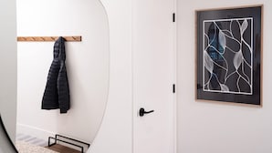 Eine weiße Tür mit schwarzem Griff, ein gerahmtes abstraktes Kunstwerk an der Wand und ein Mantel an einem Holzgestell.