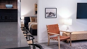 Eine moderne Küche mit schwarzer Arbeitsplatte und Holzregalen, ein Essbereich mit langem Tisch und Stühlen, eine Holzschrank und ein gerahmtes Bild an der Wand.