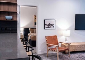 Una cucina moderna con un piano di lavoro nero e mensole in legno, un'area pranzo con un tavolo lungo e sedie, un armadietto in legno e un quadro incorniciato appeso al muro.