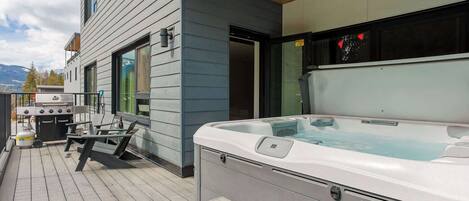 A hot tub on a wooden deck, a grill, and a patio table.