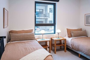 Un dormitorio con dos camas, una ventana y mesitas de noche con lámparas.