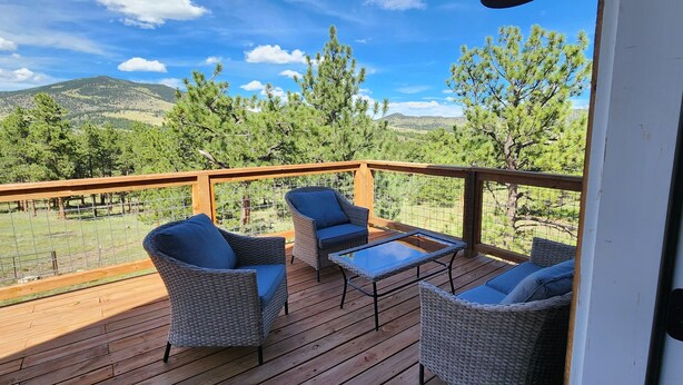 Eine Holzterrasse mit Korbmöbeln und einem Glastisch, mit Blick auf eine gebirgige Landschaft.
