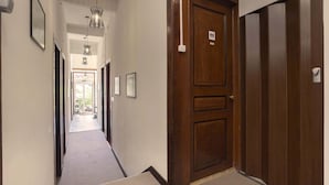 A hotel hallway with a wooden door marked for a men's restroom, a framed picture on the wall, and a hanging light fixture. - Happy Holiday Sintra (Sintra)