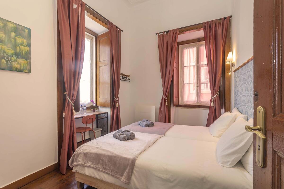 Quarto com duas camas, uma escrivaninha e uma cadeira.
