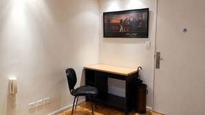 Habitación de esquina con escritorio, silla y un cuadro en la pared.
