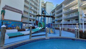 A pool area with a water slide and play structures, surrounded by multi-story buildings with balconies. - Waterfront, Harbourside, Water Park, Beach, #6615 (Indian Rocks Beach)