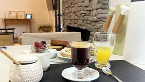 Una mesa de desayuno con una taza de café, un vaso de zumo de naranja, un tarro de mermelada y un pastel pequeño.