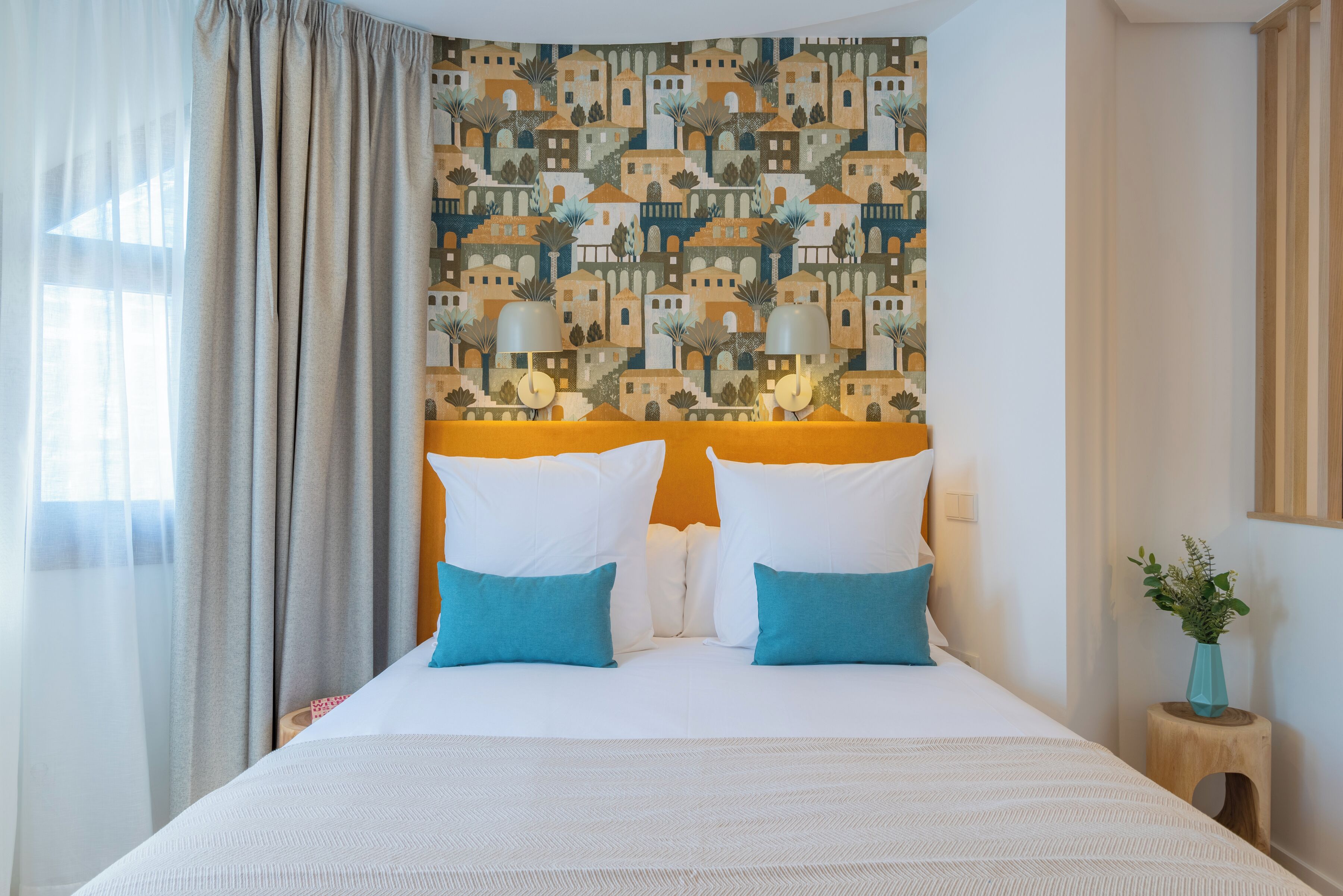 Una habitación de hotel con una cama grande, dos lámparas de noche, un papel tapiz estampado y una ventana con cortinas.