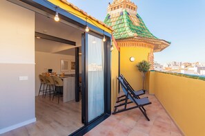 A balcony with a yellow wall, a green-roofed structure, and a sliding glass door leading to a dining area with chairs and a table. - Feelathome Atarazanas Apartments (Málaga)