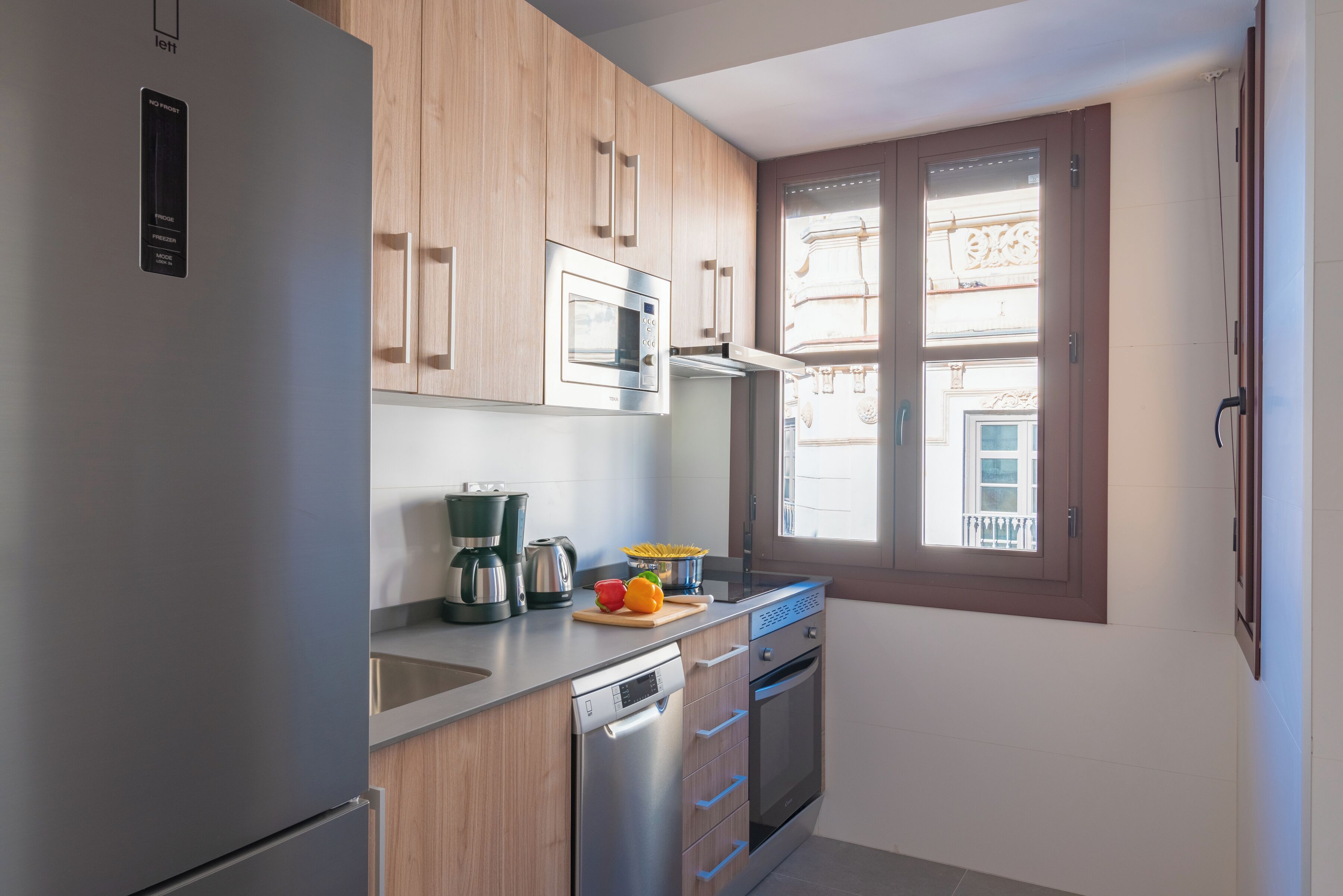 A modern kitchen with stainless steel appliances, wooden cabinets, and a window with a view of the outside.