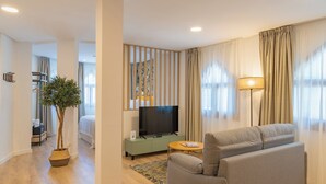 A modern living room with a grey sofa, a television on a green cabinet, a small round table, and a potted plant. - Feelathome Atarazanas Apartments (Málaga)