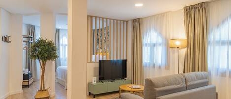 A modern living room with a grey sofa, a television on a green cabinet, a small round table, and a potted plant.