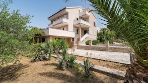 A multi-story building with balconies, surrounded by greenery and a stone pathway. - Apartment Ljubica with nice garden 2 (Novalja)