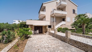 A multi-story residential building with a stone-paved courtyard, outdoor seating, and a staircase leading to the upper floors. - Apartment Ljubica with nice garden 2 (Novalja)