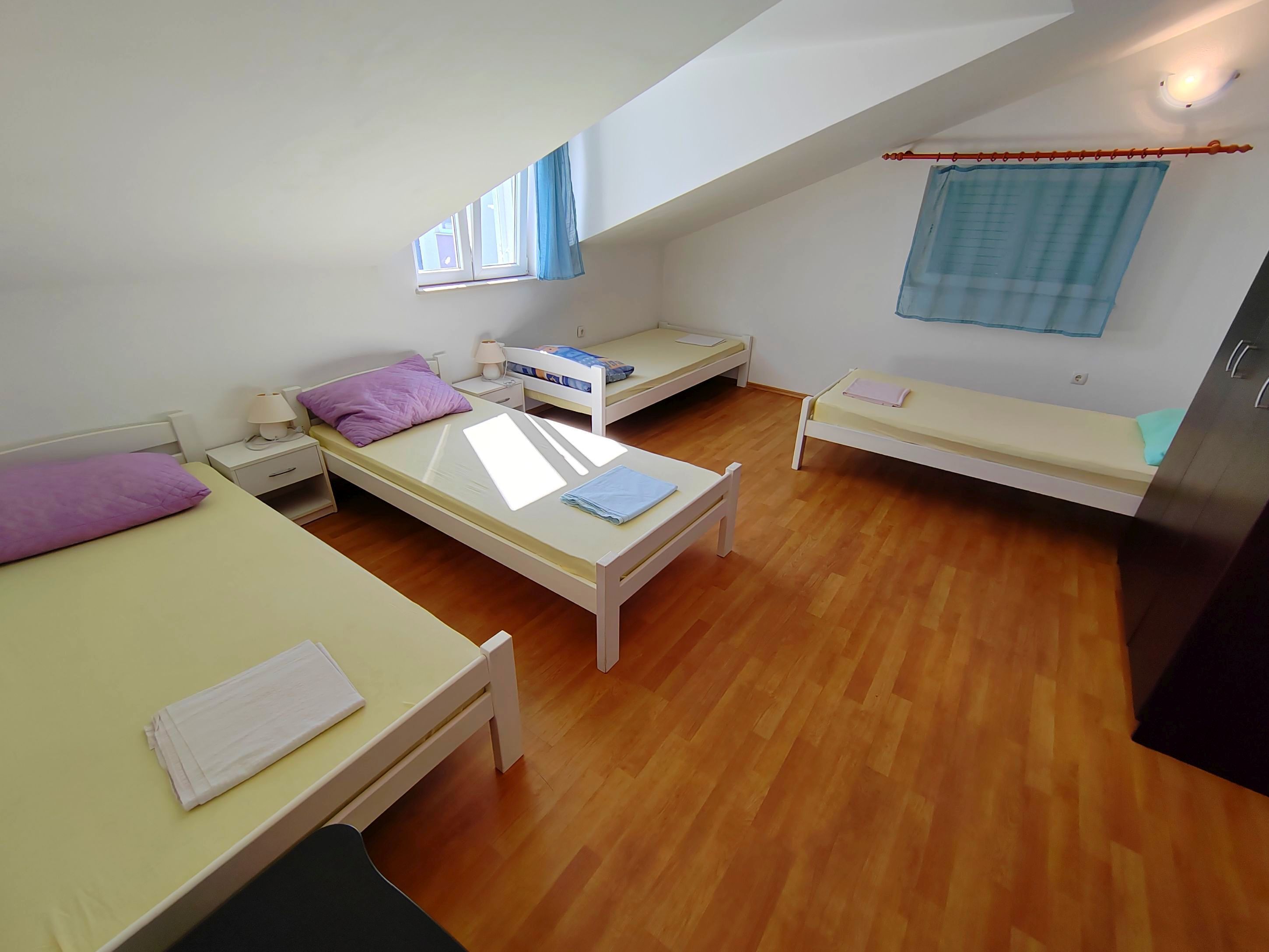 Ein Schlafsaalzimmer mit drei Einzelbetten, Holzboden, einem fenster mit Vorhängen und einer Deckenleuchte.