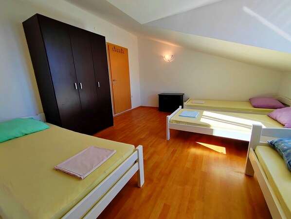 A dormitory room with two single beds, a wardrobe, a small table, and a wall-mounted light fixture.