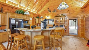 A wooden cabin kitchen with a central island, bar stools, wooden cabinets, and a hanging light fixture. - Deer's Lair Cabin in Cedar Falls Resort - 4 bedroom, 3.5 bathroom, game room (Sevierville)