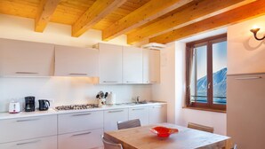 A modern kitchen with white cabinets, a wooden dining table, and a window with a mountain view.