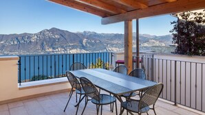 A balcony with a table and chairs, overlooking a mountainous landscape.