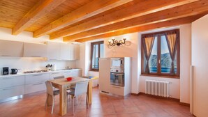 A modern kitchen with white cabinets, a wooden dining table, and a view of mountains through large windows.