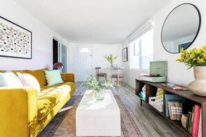 A modern living room with a yellow sofa, a white coffee table, and a bookshelf. - MUSICAL HAVEN|KARAOKE STAGE|JUKEBOX|INSTRUMENTS+! (Tempe)
