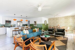 A modern living room with a sofa, chairs, and a coffee table. There is a kitchen area with a refrigerator, microwave, and island. - MUSICAL HAVEN|KARAOKE STAGE|JUKEBOX|INSTRUMENTS+! (Tempe)