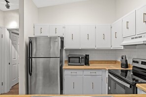 A kitchen with white cabinets, stainless steel appliances, and a wooden countertop.