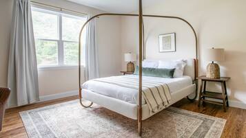 A four-poster bed with a white and green color scheme, a small bedside table with a lamp, and a large window with curtains.