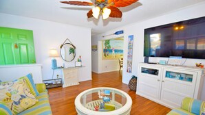 A cozy living room with a round coffee table, striped sofas, a television, and a green door.