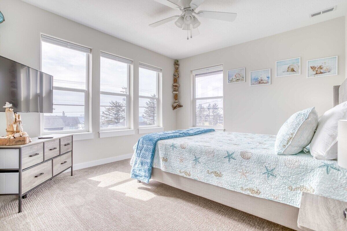 Une chambre à coucher avec un lit, une commode, un ventilateur de plafond et de grandes fenêtres.