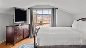 A bedroom with a large bed, a dresser, a television, and a window with a view of mountains.