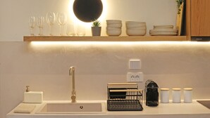 Une cuisine au design moderne, équipée d’un évier, d’un robinet, d’une machine à café et d’une étagère contenant divers objets, notamment des verres et des bols.